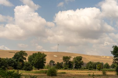 Ortasında uzun bir sopa olan bir tarla. Gökyüzü bulutlu ve güneş parlıyor
