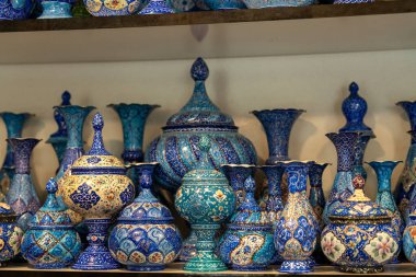 Mavi vazo ve kaselerle dolu bir raf. Vazolar farklı şekil ve boyutlarda ve hepsi de mavi.