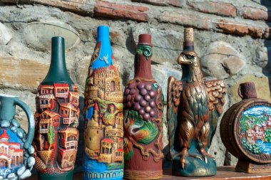 İçinde kartal olan bir vazo ve çeşitli tasarımlar olan bir şişe koleksiyonu. Vazolar ve şişeler bir masada sergileniyor, bazıları diğerlerinden daha uzun.