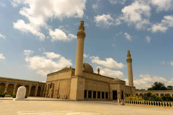İki yüksek kulesi ve tepesinde kubbesi olan büyük bir bina. Bina bir avluyla çevrili ve bir sürü penceresi var. Gökyüzü açık ve güneş parlıyor.