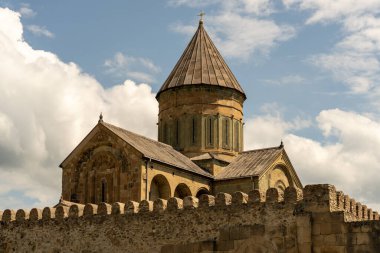 Çan kulesi ve tepesinde haç olan büyük, eski bir bina. Bina taştan bir duvarla çevrili.