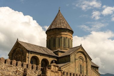 Çan kulesi ve tepesinde haç olan büyük, eski bir bina. Bina taştan bir duvarla çevrili.