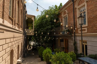 Önünde balkon ve ağaç olan tuğla bir bina. Balkon ışıklarla aydınlandı.