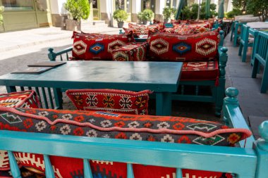 Masası ve sandalyeleri olan mavi ve kırmızı bir oturma alanı. Sandalyeler renkli yastıklarla kaplı ve masa boş.