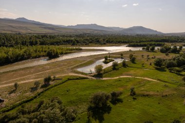 Bir nehir yemyeşil bir vadiden geçiyor. Gökyüzü açık ve güneş parlıyor.