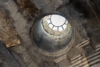 Üzerinde pencere olan taş bir duvarda küçük bir delik. Pencere yuvarlak ve üzerinde bir saat var. Delik duvarın ortasında ve taşlarla çevrili.