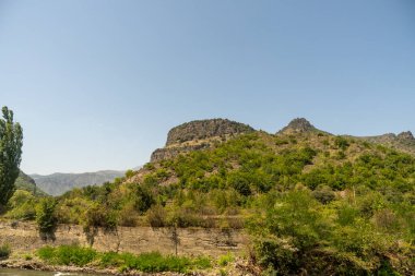 Önünde duvar olan bir dağ sırası. Duvar taştan yapılmıştır ve yemyeşil bir ormanla çevrilidir. Gökyüzü açık ve mavidir, ve güneş parlıyor. Huzur dolu bir sahne.