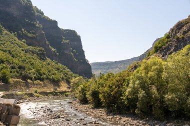 Her iki tarafında ağaçlar olan bir vadi boyunca bir nehir akar. Su berrak ve gökyüzü mavi.