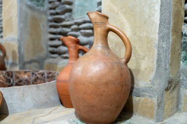 Kahverengi bir vazo başka bir vazonun yanında bir çıkıntıda duruyor. Vazo eski ve kırsal bir görünüme sahip.