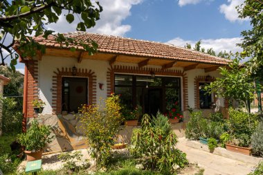 Kırmızı çatılı ve beyaz duvarlı küçük bir ev. Evin ön bahçesinde bir sürü çiçek ve bitki var.