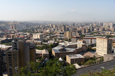 Arkasında dağ olan bir şehir manzarası. Şehir yüksek binalarla dolu ve bir sürü yeşil ağacı var.