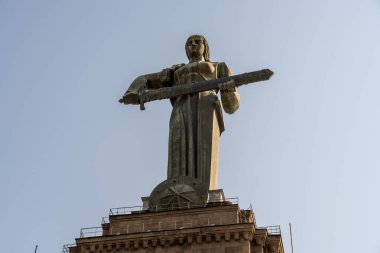 Kılıç tutan bir kadın heykeli. Heykel uzun ve metalden yapılmıştır. Gökyüzü açık ve mavi