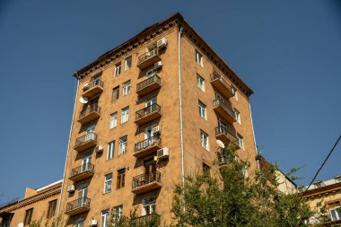 Arka planda mavi gökyüzü ve balkonları olan kahverengi bir bina. Bina yüksek ve birçok penceresi var.