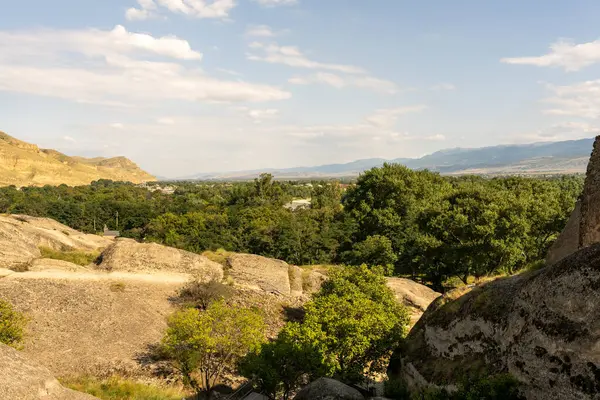 Önünde orman olan bir dağ sırası. Gökyüzü açık ve güneş parlıyor.