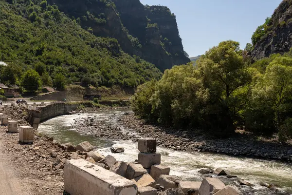 Kayalık bir kıyı şeridi ve arkasında bir köprü olan bir nehir. Su berrak ve sakin.