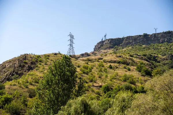 İçinden elektrik hattı geçen bir dağ. Güç hattı siyah ve gökyüzü mavi.