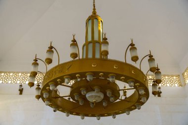 Altından çok sayıda ışık sarkan bir altın ve beyaz avize. Avize süslenmiş ve dini bir teması var.