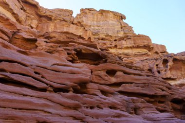 Arka planda mavi gökyüzü olan kayalık bir uçurum. Uçurum deliklerle dolu ve pürüzlü bir dokusu var.