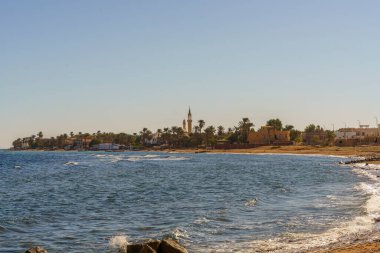 Arkasında küçük bir kasaba olan güzel bir sahil. Su sakin ve gökyüzü berrak.