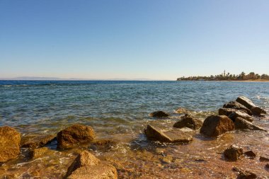 Okyanus sakin ve gökyüzü açık. Kıyıdaki kayalar büyük ve dağınık.