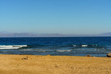 Arkasında kumlu bir plaj olan güzel mavi bir okyanus. Gökyüzü açık ve güneş parlıyor.