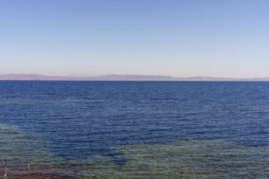Okyanus sakin ve mavidir. Gökyüzünde birkaç beyaz bulut vardır. Su derin ve göz alabildiğince uzanıyor.