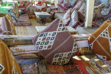 Bir sürü yastıklı bir oda ve üzerinde kitap olan bir masa. Yastıklar renkli ve rahat bir atmosfer yaratacak şekilde düzenlenmiş.