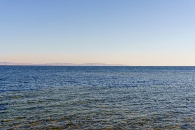 Okyanus sakin ve berrak, görünür dalgalar ya da dalgalar yok. Gökyüzü parlak mavi, görünürde bulutlar yok. Huzurlu ve huzurlu bir sahne.