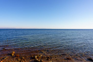 Okyanus sakin ve gökyüzü açık. Su koyu mavi bir renktir. Kıyıdaki kayalar kahverengi ve su sakin.