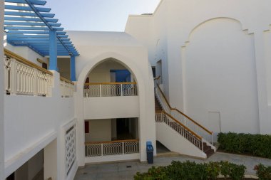 Mavi kemerli ve balkonlu beyaz bir bina. Balkonun mavi bir tentesi var.