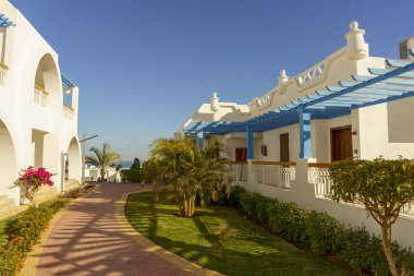 Mavi çatılı ve beyaz duvarlı bir yürüyüş yolu. Geçit ağaçlar ve çalılarla kaplı.