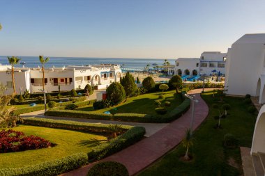 Büyük bir çimleri ve yürüyüş yolu olan deniz kıyısındaki bir tatil köyü. Çimen yemyeşil ve yürüyüş yolu tuğladan yapılmıştır. Bölgeye dağılmış birkaç saksı bitkisi var.