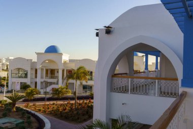 Mavi kubbeli ve mavi kemerli beyaz bir bina. Kemer yolu açık ve bir balkon var.