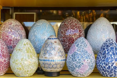 Renkli yumurta şekilli vazolar sergileniyor. Vazolar camdan yapılmış ve eşsiz, sanatsal bir tasarıma sahip. Ekran, renk çeşitliliğini vurgulayacak şekilde düzenlenmiştir