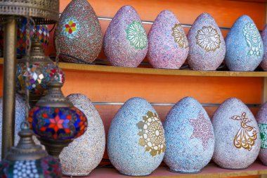 Rafta renkli yumurta şekilli vazolar sergileniyor. Vazolar farklı boyutlarda ve renklerde, ve onları bir grup yumurta gibi gösterecek şekilde sıralanmış.