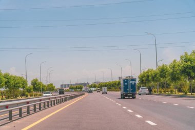 Mavi bir kamyonet yolda ilerliyor. Yolda birkaç araba ve kamyon var. Gökyüzü açık ve mavi