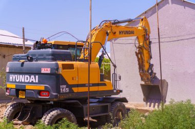 Sarı ve siyah bir Hyundai inşaat aracı. Çukur kazıyor. Araç toprak bir yolda.
