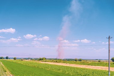 Arka planda elektrik hattı olan bir alan. Gökyüzü mavi ve berrak. Uzakta bir kasırga var.