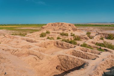 Ortasında büyük bir tümsek olan bir çöl manzarası. Höyük toprak ve çimlerle çevrili.