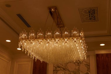 Tavandan sarkan büyük, süslü bir avize odanın üzerine sıcak bir parıltı saçıyor. Avize kristalden yapılmıştır ve birçok parçaya sahiptir. Parıltılı bir etki yaratır. Oda iyi aydınlatılmış.