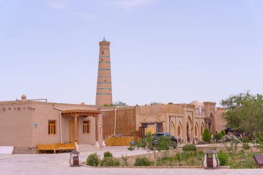 Önünde kule ve araba olan bir bina. Bölgede dolaşan insanlar var.