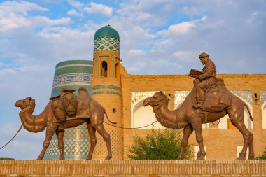 Binanın önünde bir adam devenin üzerinde oturuyor. İki deve var, biri insan taşıyor.