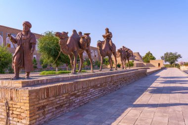 Elinde kitap tutan bir adamın heykeli tuğla bir duvardadır. Duvarda üç deve heykeli var.