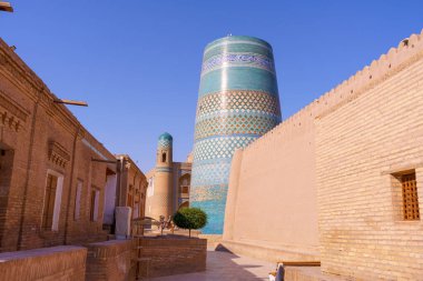 Ortasında mavi ve beyaz kule olan bir bina. Bina tuğla bir duvarla çevrili.