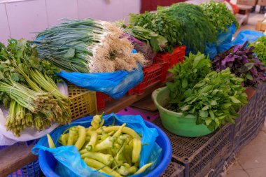Biber, soğan ve yeşilliklerle dolu bir masa. Sebzeler plastik torbalar ve kaplarda.