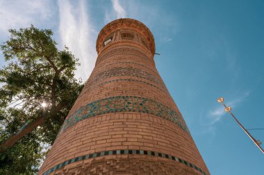 Mavi çizgili uzun bir tuğla kule. Kule bir şehrin ortasındadır. Gökyüzü mavi ve berrak