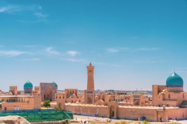 Yüksek kulesi ve mavi kubbesi olan bir şehir. Gökyüzü mavi ve berrak. Etrafta dolaşan bir sürü insan var.