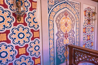 Duvar güzel mavi ve sarı bir dizaynla süslenmiş. Karmaşık desenler ve renkler görsel olarak çarpıcı ve eşsiz bir atmosfer yaratıyor. Duvar tavanlı bir odada.