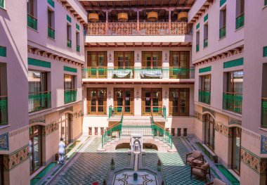 Ortasında çeşme olan bir avlu. Avluda birkaç sandalye ve bir bank var.