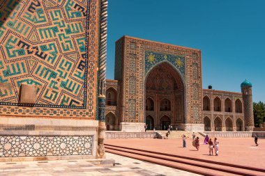 Bir grup insan mavi kemerli bir binanın önünde yürüyorlar. Bina mavi ve beyaz fayanslarla süslenmiş.